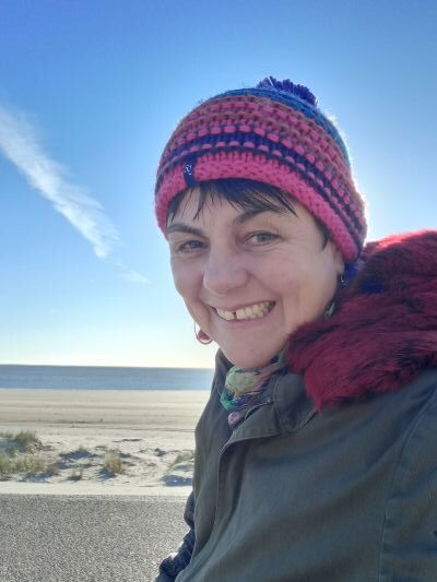 Eine Frau, winterlich gekleidet, vor dem Hintergrund eines Strandes.