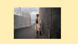 Ilona Clemens steht nachdenklich zwischen einer weißen Kalkmauer und einer dunklen Steinwand mit Blick aufs Meer, Symbolbild für Struktur und Übergang