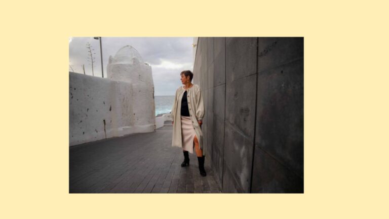 Ilona Clemens steht nachdenklich zwischen einer weißen Kalkmauer und einer dunklen Steinwand mit Blick aufs Meer, Symbolbild für Struktur und Übergang